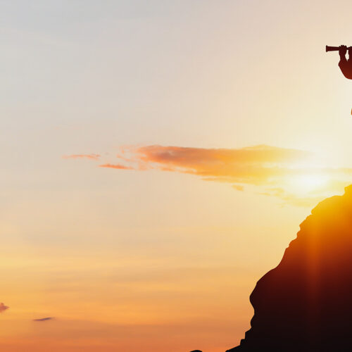 silhouette of a man using spyglass on mountaintop